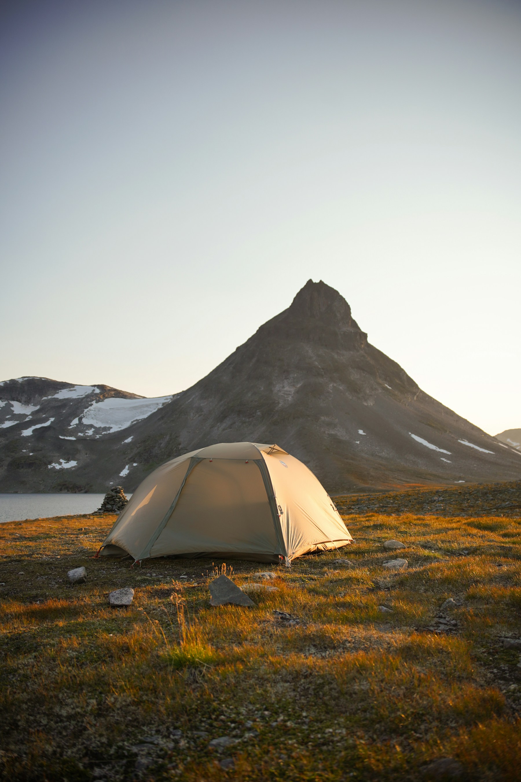 Ett tält i ett öppet fjällandskap i varmt morgonljus.